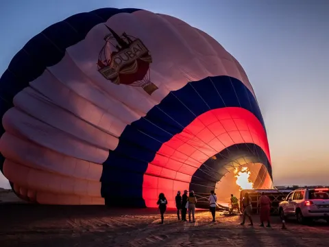 Hot air balloon over Dubai desert dunes at sunrise with passengers in the basket