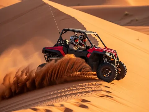Pair of Polaris RZR dune buggies riding across a Dubai desert dune face