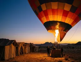 Hot air balloon inflating at dawn beside a row of camp tents